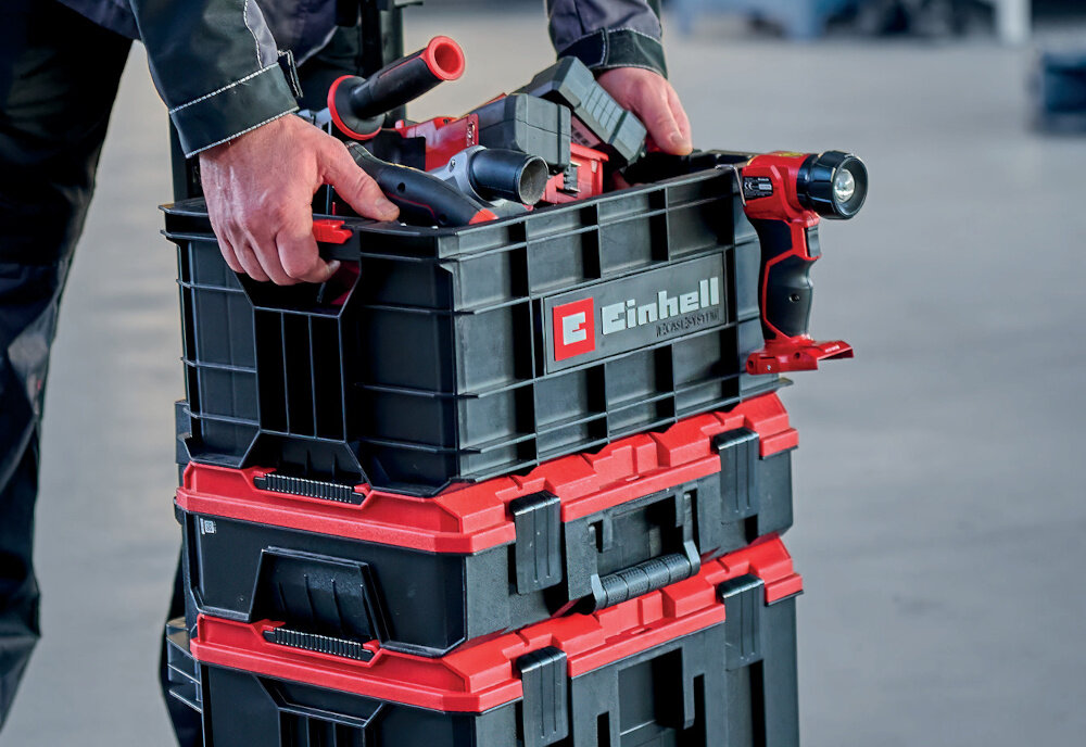 Skrzynka na narzędzia EINHELL E-Case 4540037 pomieszczenie plac budowy osoba umieszcza skrzynkę na innych skrzynkach waga 2,7 kg dwa ergonomiczne uchwyty boczne wymiary 45,6 × 34,2 × 23 cm