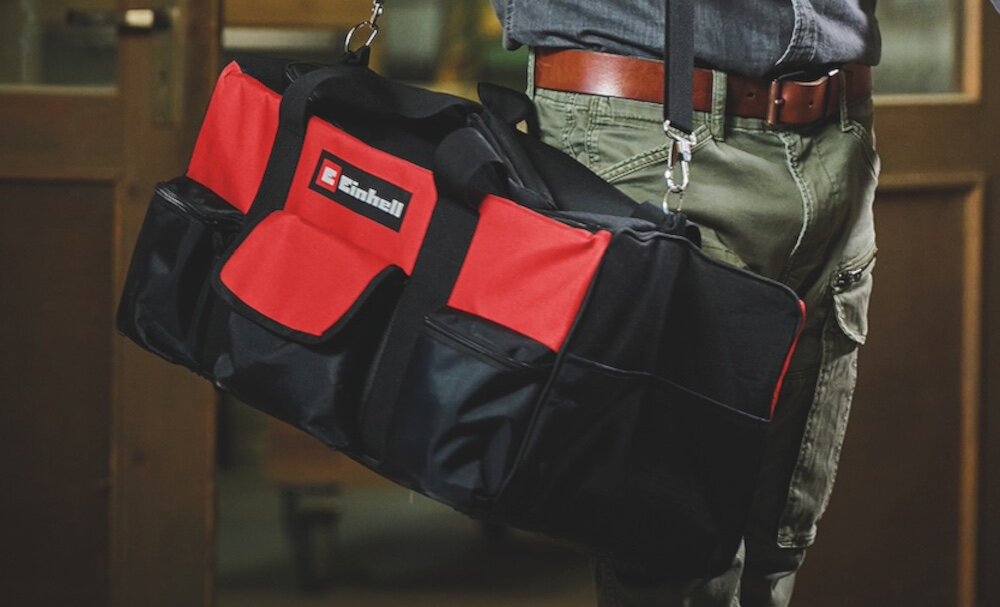 Torba narzędziowa EINHELL 4530078 pomieszczenie warsztat osoba niesie torbę na ramieniu w tle drewniane drzwi praktyczna mobilność transport przenoszenie przechowywanie