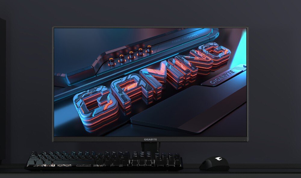 Monitor GIGABYTE GS27FA Obraz monitora wyświetlającego trójwymiarowy napis 'GAMING' z efektem świetlnym w kolorach czerwonym i niebieskim. Na biurku znajduje się klawiatura, myszka i monitor marki GIGABYTE, ustawiony na ciemnym tle, opis
