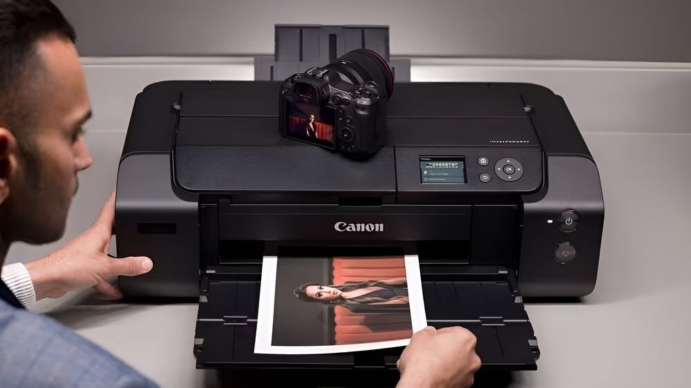 Drukarka CANON ImagePROGRAF PRO-310 Druk w kolorze, Wi-Fi drukarka postawiona na biurku w studiu mężczyzna wyciągający wydrukowane zdjęcie odbitki artystyczne odporność na światło
