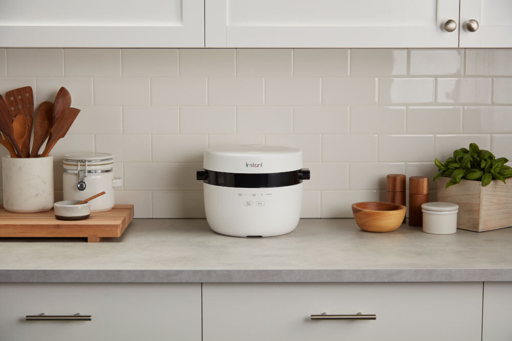 Ryżowar INSTANT POT Multigrain ryżowar stoi na kuchennym blacie tło kuchenne jasne szafki urządzenie w kolorze białym czarne elementy funkcja opóźnionego startu utrzymywanie ciepła nawet do 10 godzin zaplanowanie gotowania na wybraną godzinę ciepły, świeży posiłek dla osób zapracowanych posiłki gotowe na czas