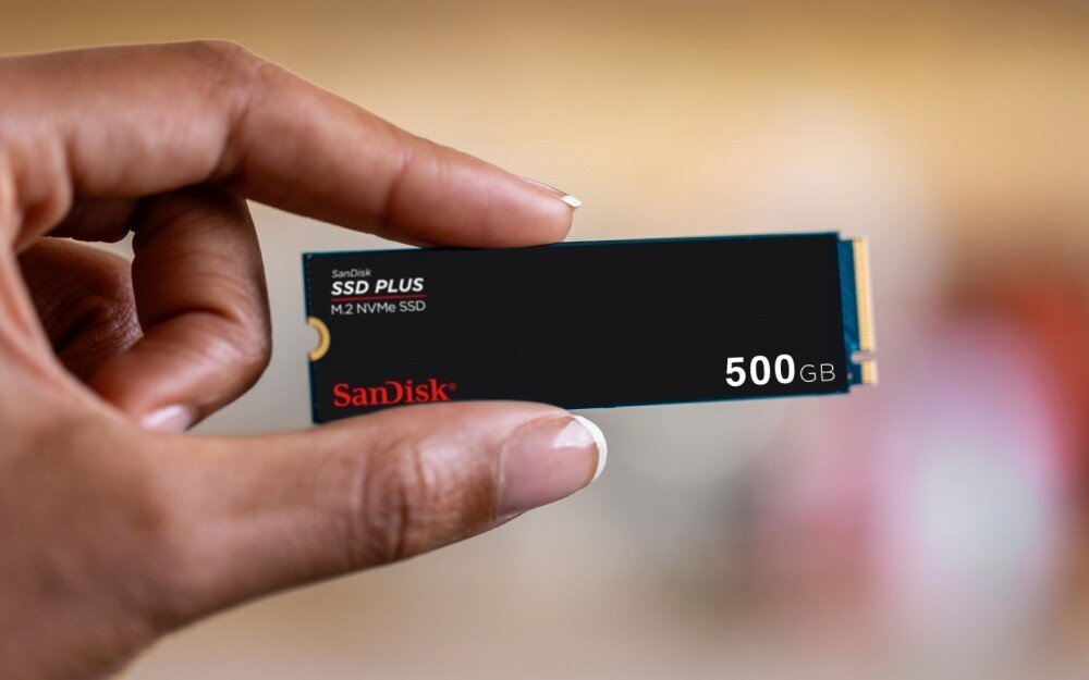 Dysk SANDISK Plus Zbliżenie dłoni trzymającej wąski dysk M.2, tło jest rozmyte, format, wielkość, konstrukcja, oprogramowanie