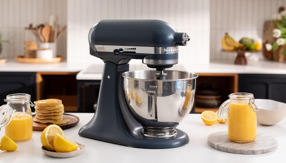 Robot kuchenny planetarny KITCHENAID Artisan 5KSM95PSEBS 275W niebieksi robot stoi bokiem na blacie srebrna misa suwak na obudowie pomarańczowa masa w słoikach z wytrzymałego odlewu cynkowego stabilność urządzenia regulacja prędkości od 58 do 220 obrotów na minutę dostosowanie pracy miksera waży około 10,5 kg długość przewodu zasilającego wynosząca 114 cm dla amatorów i doświadczonych kucharzy