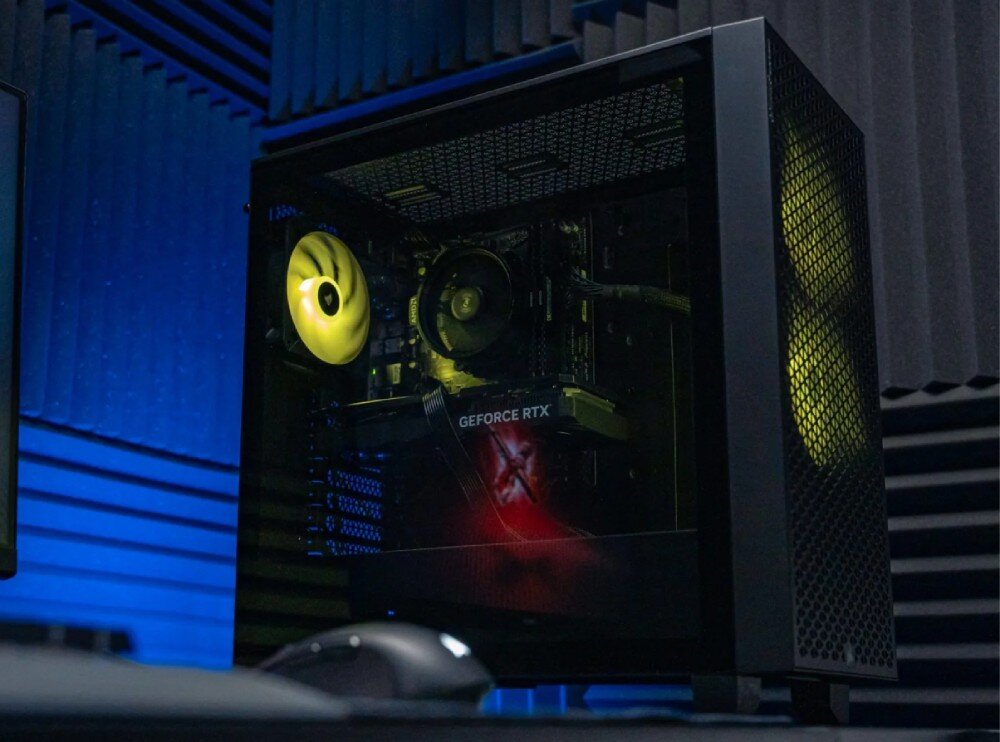 Komputer OPTIMUS E-Sport GA520T-CR5 Obudowa komputera z podświetlonym wnętrzem, widoczne wentylatory w kolorze żółtym oraz karta graficzna z napisem GeForce RTX, ustawiona w pomieszczeniu z panelami wygłuszającymi, opis