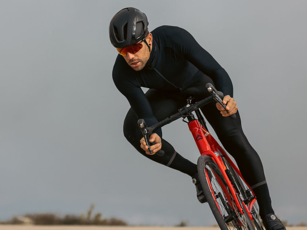 Kolarz szosowy w pochylonej pozycji aerodynamicznej na czerwonym rowerze, mający na sobie kask Lazer Vento.