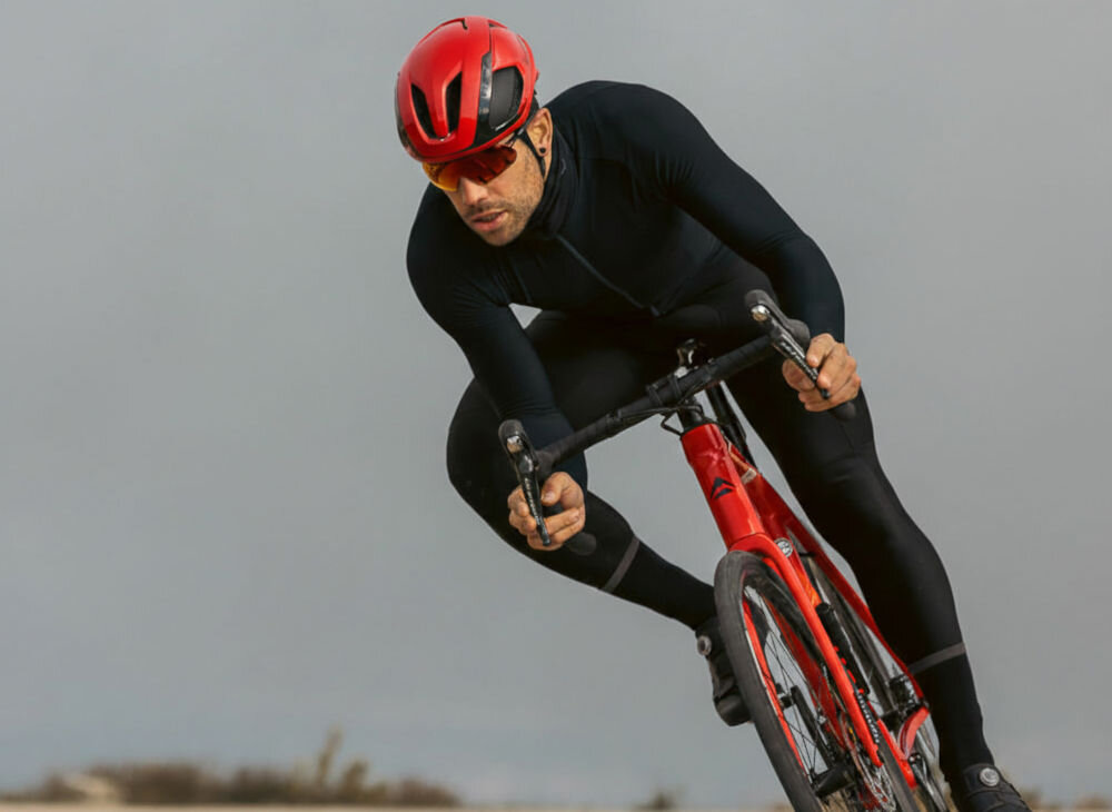 Kolarz szosowy w pochylonej pozycji aerodynamicznej na czerwonym rowerze, mający na sobie kask Lazer Vento.