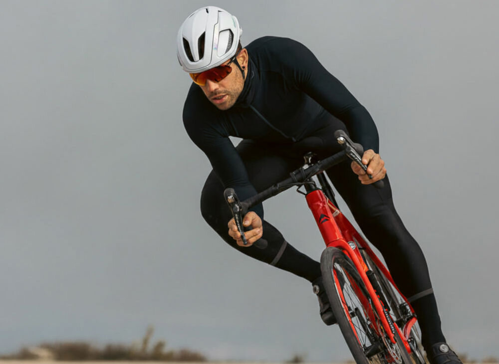 Kolarz szosowy w pochylonej pozycji aerodynamicznej na czerwonym rowerze, mający na sobie kask Lazer Vento.