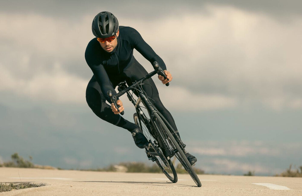 Kask rowerowy LAZER Strada KinetiCore Czarny Szosowy (rozmiar S) droga ulica szosa osoba w kasku jedzie na rowerze w tle niebo bezpieczeństwo komfort wsparcie