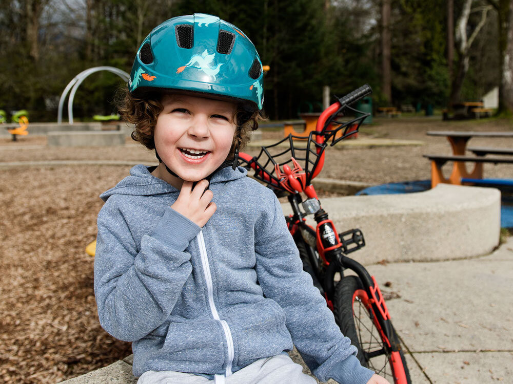 Kask rowerowy LAZER Nutz KinetiCore 2.0 Zielony dla Dzieci (rozmiar 50-56) park plac zabaw dziecko w kasku siedzi na ławce patrzy przed siebie uśmiecha się w tle drzewa ławki huśtawki bezpieczeństwo ochrona komfort bezpieczna jazda na rowerze
