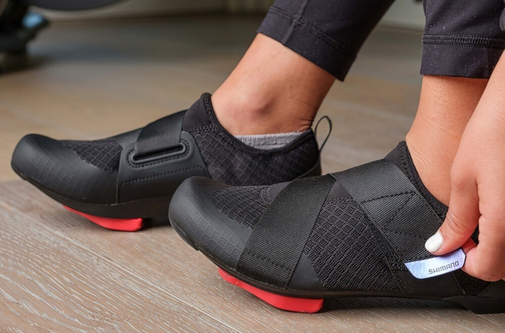 Buty rowerowe SHIMANO SH-IC100 Czarny rozmiar 39 osoba ubiera buty na stopy podłoga praktyczne paski na rzepy stabilność komfort noszenia stopa leży pewnie w bucie kontrola zapobiega przesuwaniu się stopy