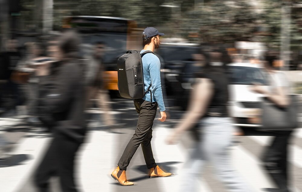 Plecak UNISTELLAR ACBP001 do teleskopów Odyssey-Odyssey Pro  człowiek z plecakiem idzie zatłoczonym chodnikiem  