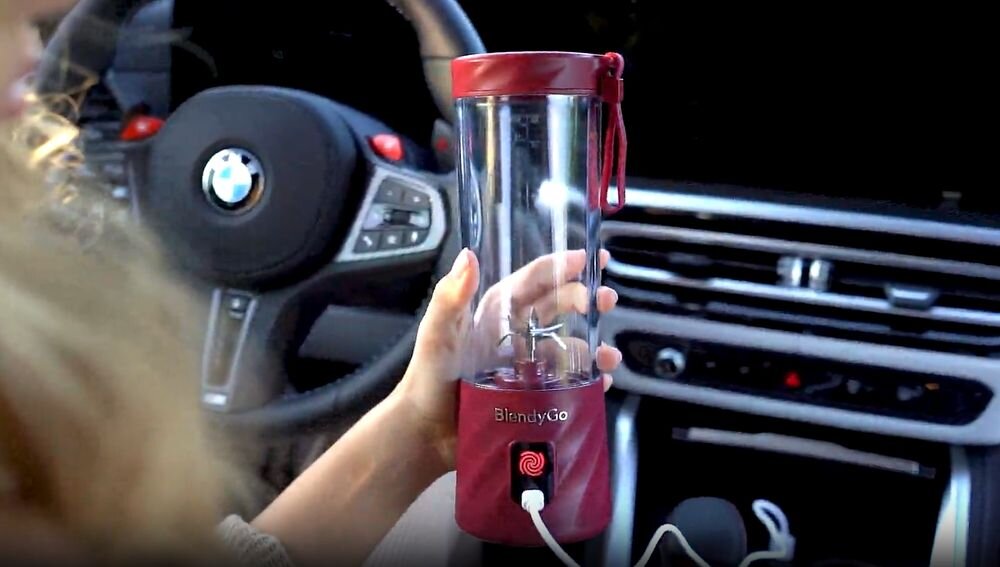osoba trzymająca blender w ręku podłączony do gniazda USB w samochodzie