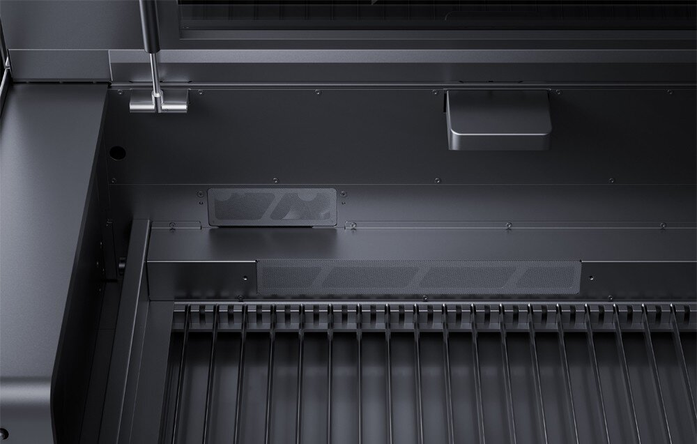 Wnętrze urządzenia z metalowymi elementami i kratką, prawdopodobnie część grawerki laserowej. Widoczne są detale konstrukcyjne i mechaniczne.