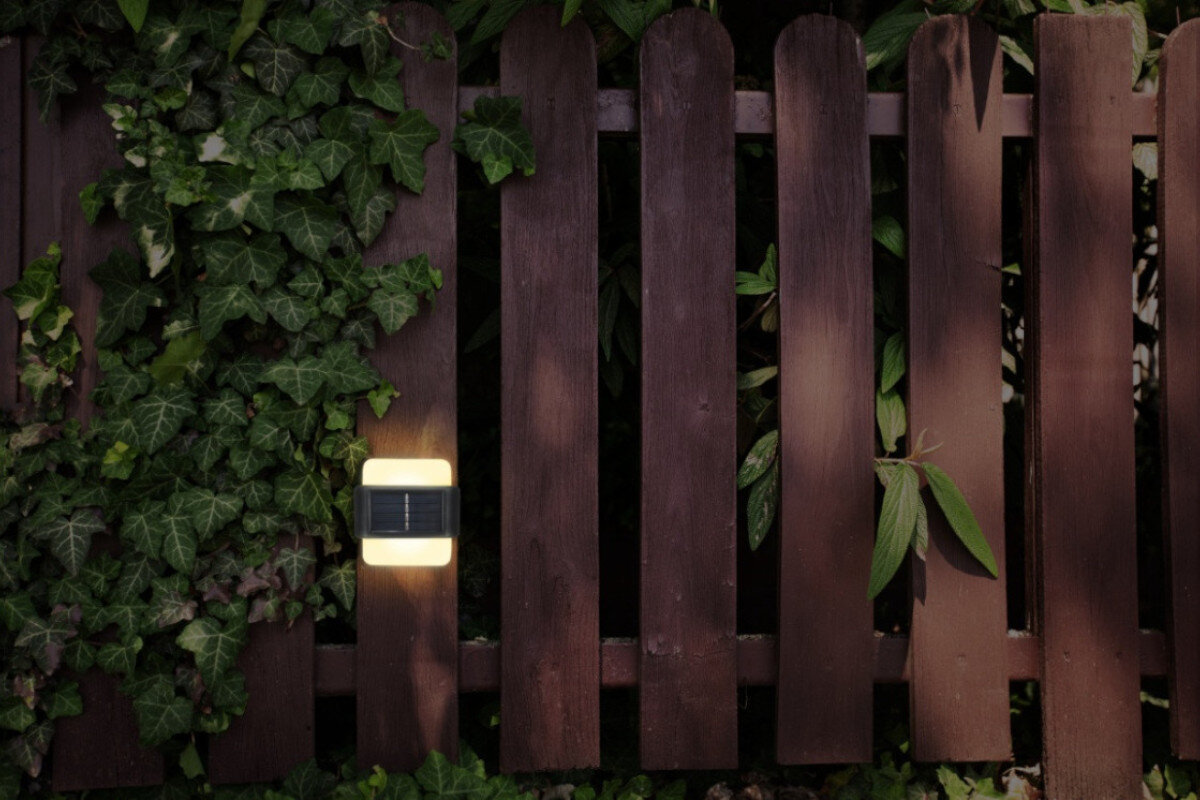 Kinkiet zewnętrzny solarny EXTRALINK Arras EX.24992 Czarny, słońce, panel, oszczędność, energia, kinkiet zamontowany do deski płotu, w tle rośliny