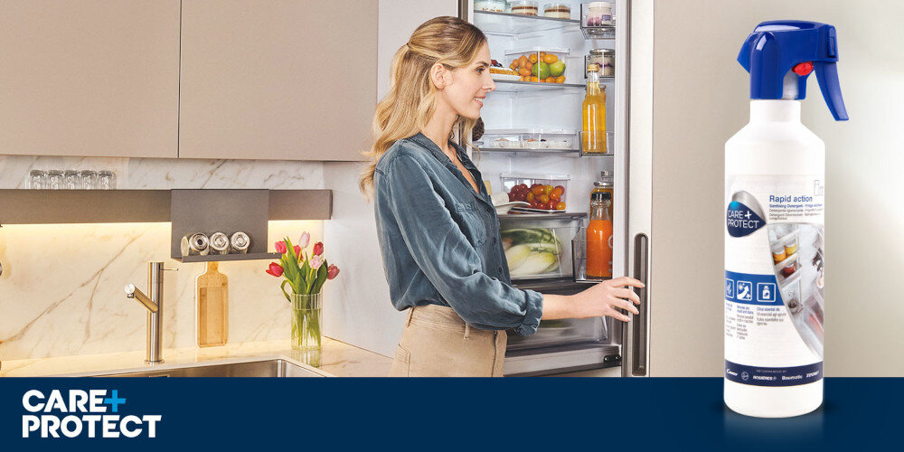 Płyn do czyszczenia Lodówek CARE+PROTECT CSL4001/1 500 ml zdjęcie lifestyle wizualizacja kobieta otwarta lodówka widoczne jasne wnętrze kuchnia meble jasne pomieszczenie preparat butelka opakowanie proste czyszczenie linia Effective Cleaning wygoda skuteczność porządek higiena świeżość