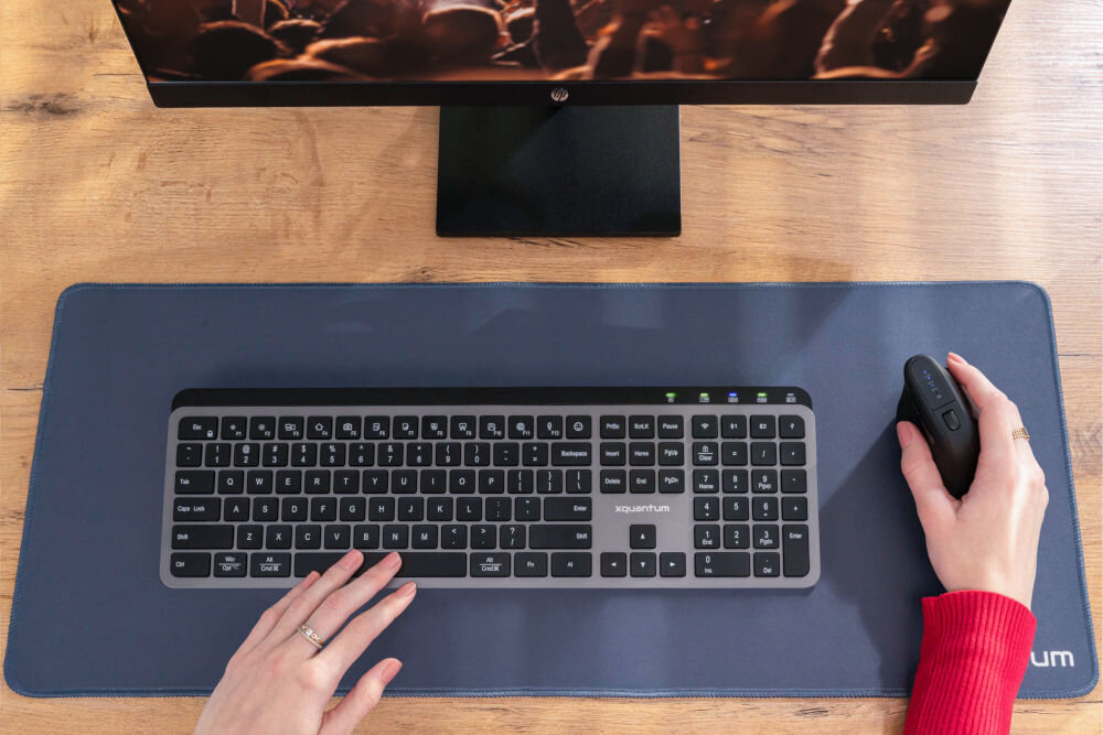 Mysz XQUANTUM WM700K Widok z góry na stanowisko pracy z czarną klawiaturą i myszą pionową XQUANTUM na dużej niebieskiej podkładce.