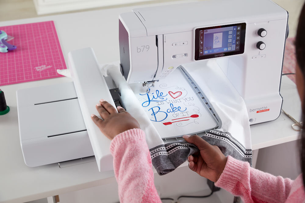 Hafciarka BERNETTE B79 + Program Bernina Creator V9 maszyna wyświetlacz pokrętła osoba haftuje napis na białym materiale pole haftu o wymiarach 260 x 160 mm duże bardziej złożone efektywne wzory mniejsze projekty wymagające większej przestrzeni roboczej 200 różnorodnych wzorów haftów kreatywne eksperymenty 7 wielowymiarowych czcionek automatyczne wykrywanie wielkości tamborka