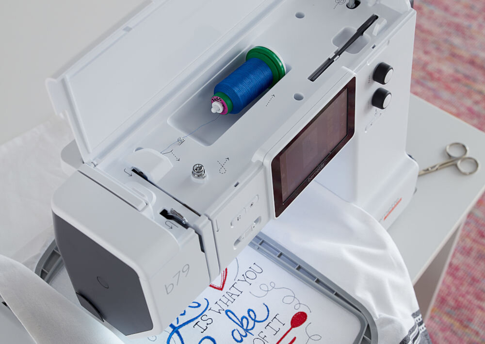 Hafciarka BERNETTE B79 + Program Bernina Creator V9 zdjęcie od góry szpulka z nitką wewnątrz obudowy maszyny napis na białym materiale wyświetlacz pokrętła System detekcji nici automatyczne wykrywanie zerwania nitki górnej brak nici w dolnej szpulce szybkie reagowanie uzupełnienie nici płynność szycia zwiększona efektywność komfort użytkowania maszyny precyzyjna i bezproblemowa praca