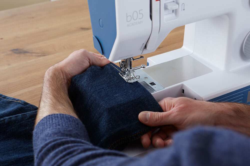 Maszyna do szycia BERNETTE 05 Academy Heavy Duty + Torba na maszynę maszyna blat osoba szyje jeans igła stopka nitka biało niebieska maszyna funkcja wolnego ramienia szycie wąskich i trudno dostępnych elementów odzieży wąska przestrzeń nasunięcie materiału równomierne dokładne prowadzenie ściegu dla początkujących i zaawansowanych krawców