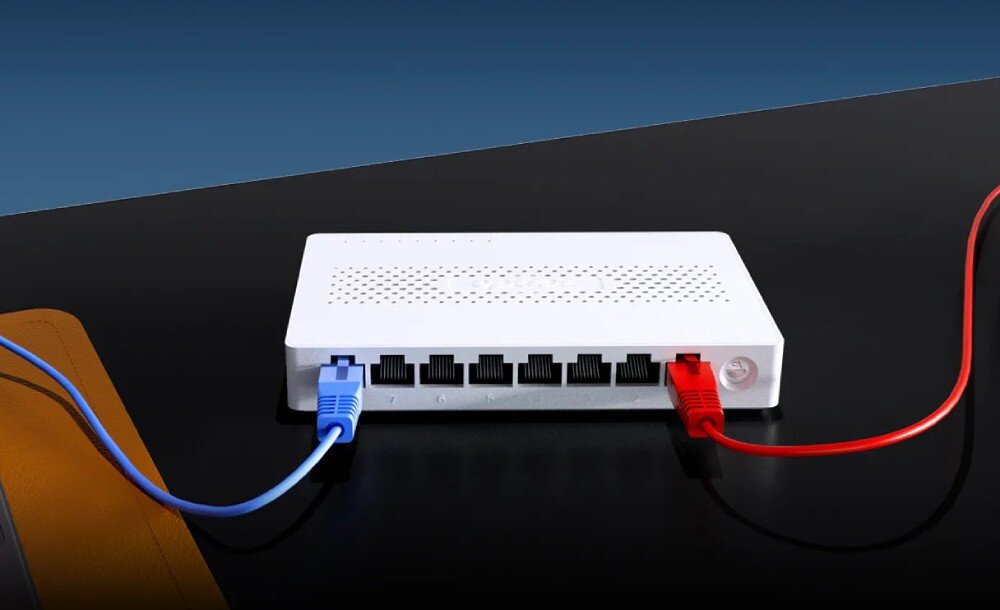 Switch TENDA SM108 Urządzenie sieciowe leżące na płaskiej powierzchni, do którego podłączone są dwa kable: jeden z lewej i jeden z prawej strony, konstrukcja, działanie, funkcje