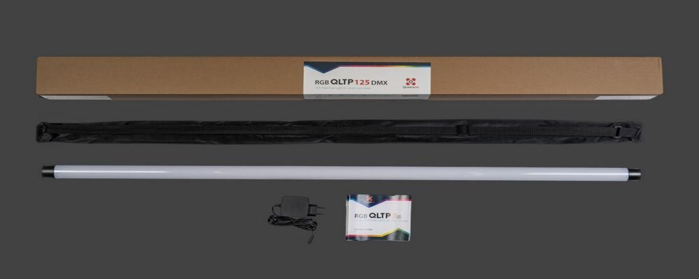 Na obrazie znajduje się lampa tuba LED z białym korpusem, czarnym etui, zasilaczem oraz instrukcją. Opakowanie kartonowe ma napis \'RGB QLTP 125 DMX\'.