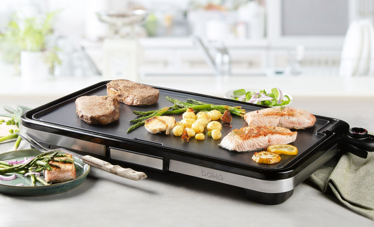 Grill DOMO Plancha XXL DO9263G, grillowanie, duże, powierzchnia, smażenie, Grill DOMO Plancha XXL DO9263G z potrawami – steki, łosoś, szparagi oraz ziemniaczki, ustawiony na blacie, jasna kuchnia