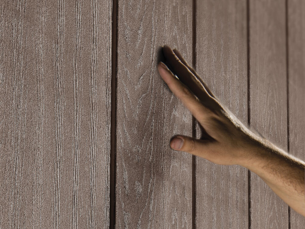 Dłoń dotyka powierzchni panelu o fakturze przypominającej drewno, w kolorze brązowym.