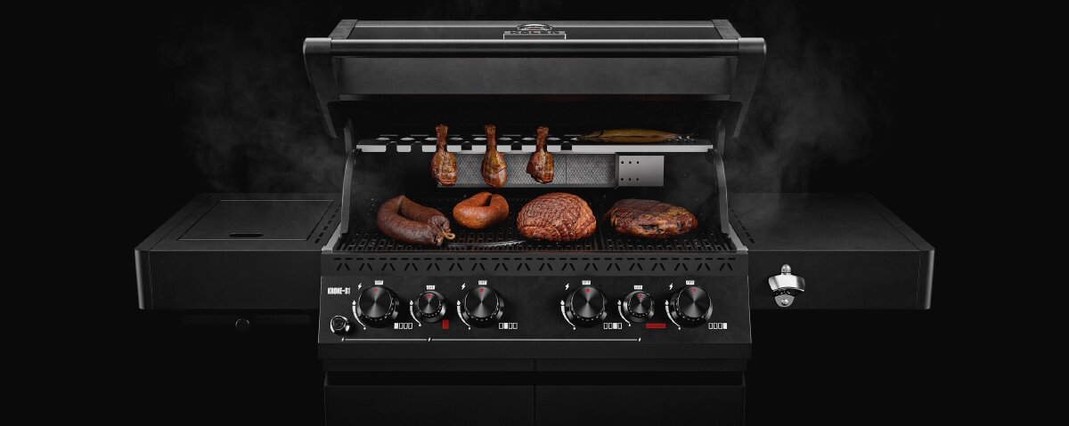 Czarny grill gazowy z otwartą pokrywą, na ruszcie znajdują się różne rodzaje mięsa. Na panelu przednim widoczne są pokrętła do regulacji temperatury oraz logo producenta.