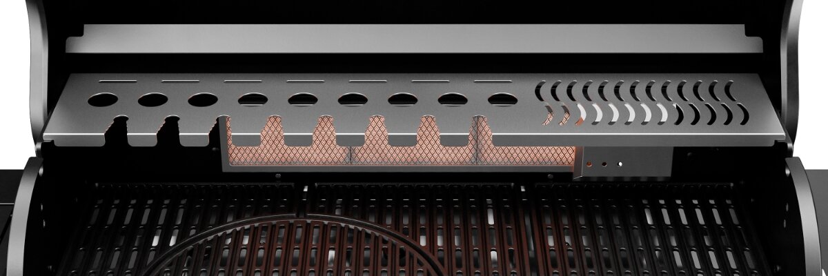 Wnętrze grilla gazowego z widocznym rusztem i metalową osłoną z otworami wentylacyjnymi. Osłona ma rząd okrągłych i podłużnych otworów oraz elementy w kształcie zębów.