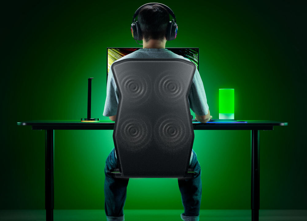 Mata haptyczna RAZER Freyja RC81-04340101-R3M1 prezentacja maty od tyłu i jej działania mężczyzna siedzący na niej przy komputerze w założonych słuchawkach na zielonym tle Razer Synapse dostosowanie reakcji haptycznej indywidualne preferencje regulacja intensywności gotowe profile