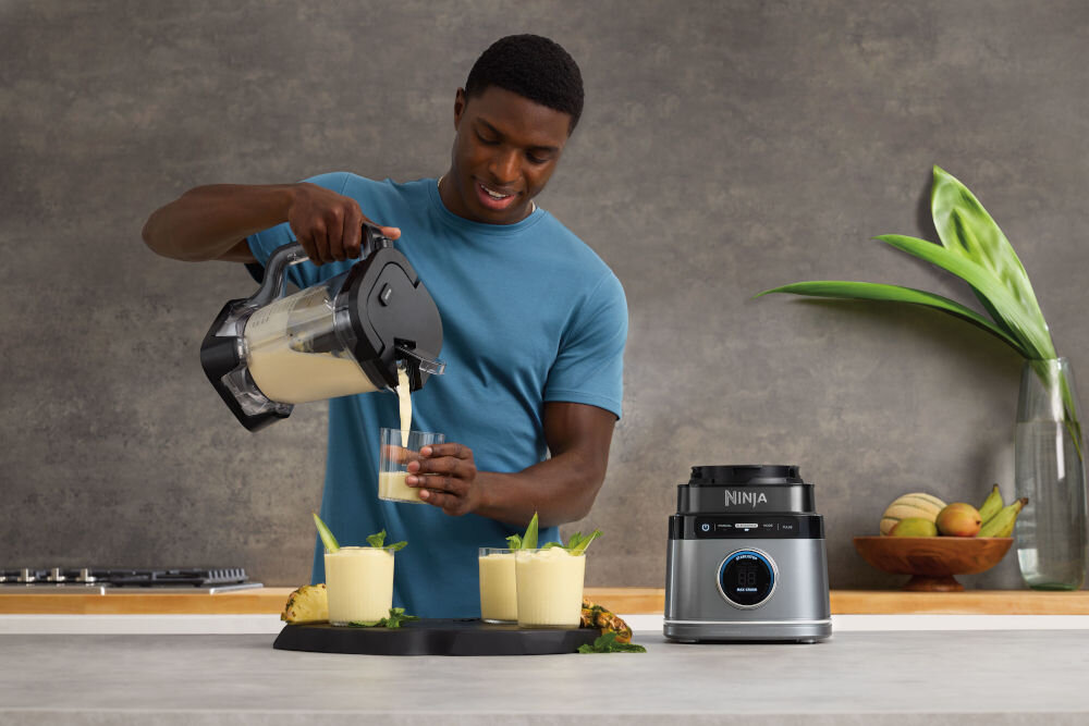 Blender kielichowy NINJA Power Blender Pro TB201EU mężczyzna przelewa jasny sok do szklanek szara podstawa blendera przyciski wyświetlacz optymalna jakość miksowania moc 1200 W błyskawiczne precyzyjne blendowanie koktajle mrożone drinki zdrowe przekąski ulubione owoce warzywa jogurty inne składniki wygoda świeżość