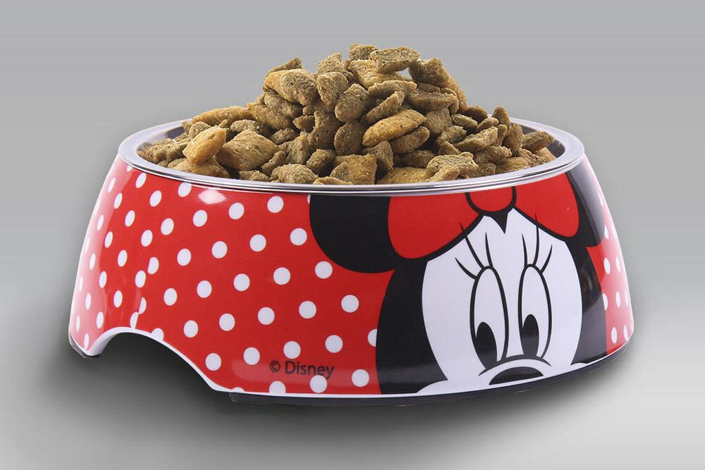 Miska dla psa CERDA Minnie, licencjonowany design Disney, żywe kolory, modny wzór dla psa, wystrój wnętrza - Na zdjęciu widoczna jest miska dla psa z motywem postaci z komiksów Minnie, obok której leży czerwony koc z białym napisem Minnie oraz zabawki w kształcie postaci z komiksów. Podłoga jest drewniana, a w tle znajduje się ciemna kanapa