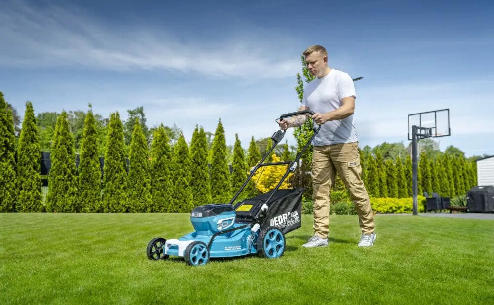 Kosiarka akumulatorowa DEDRA SAS+ALL DED6997X-2A5 ogród trawnik osoba kosi trawę w tle dom niebo drzewa kwiaty zadbany trawnik koszenie trawy mobilność zasilanie akumulatorowe