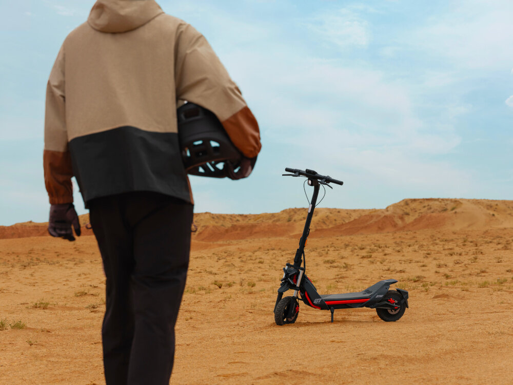 Hulajnoga elektryczna SEGWAY Ninebot ZT3 Pro D 70km 1600W Amortyzacja 11 cali Czarny piasek pustynia osoba podchodzi do hulajnogi w tle niebo do jazdy po mieście dynamiczne i ekscytujące podróżowanie szereg udogodnień i praktycznych rozwiązań moduł Bluetooth kierunkowskazy składana konstrukcja styl moc wygoda