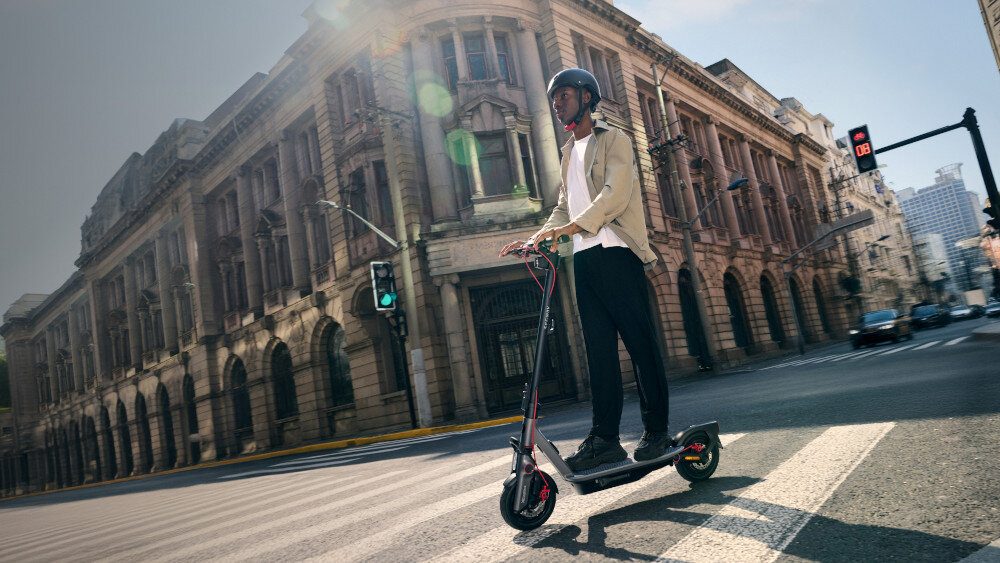 Hulajnoga elektryczna SEGWAY Ninebot F3 Pro D 70km 1200W Amortyzacja 10 cali Czarny miasto osoba jedzie na hulajnodze po drodze w tle budynki samochody niebo silnik o mocy 1200 W cicha praca i płynna kontrola prędkości pokonywanie wzniesień o nachyleniu do 24% maksymalna prędkość do 20 km/h