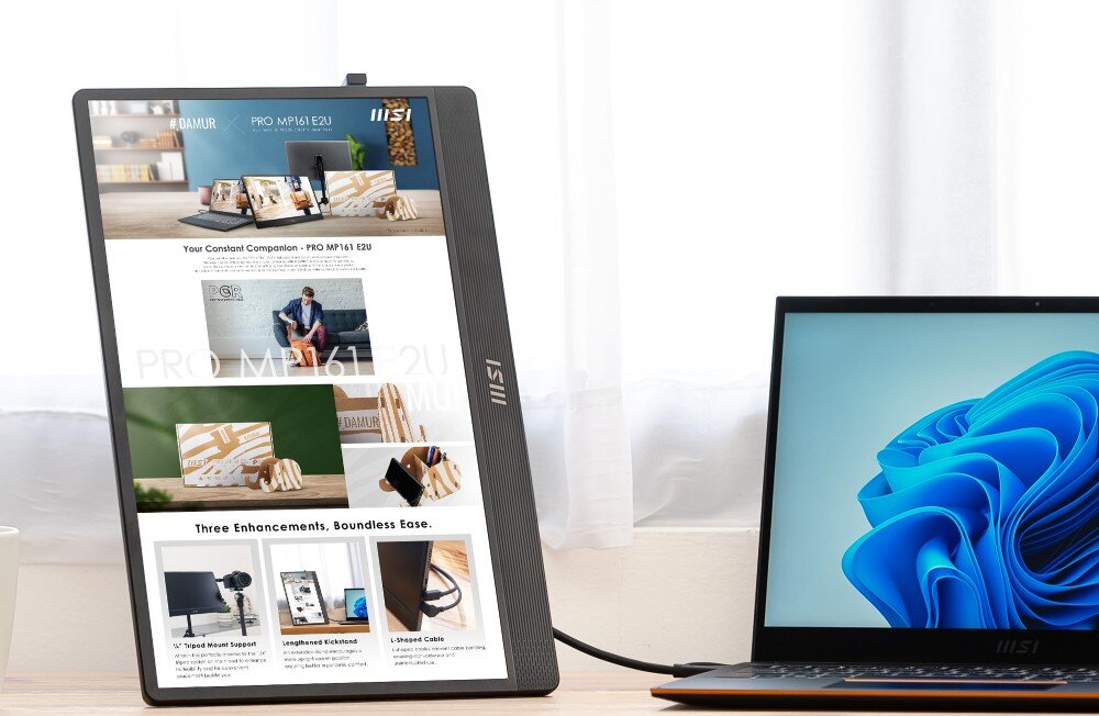 Monitor MSI Pro MP161 E2U ekran ustawiony pionowo wyświetla stronę internetową, obok znajduje się laptop z systemem Windows na tle białych zasłon, konstrukcja, waga, grubość, etui