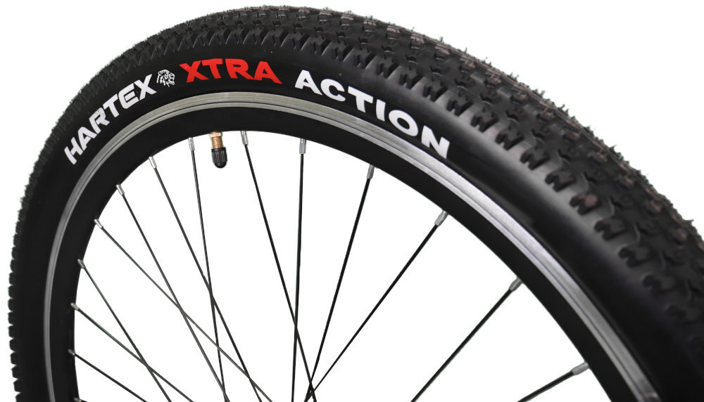 Zbliżenie na oponę rowerową z widocznym napisem \'HARTEX XTRA ACTION\'. Opona ma wyraźny bieżnik i jest zamontowana na metalowej obręczy z szprychami.