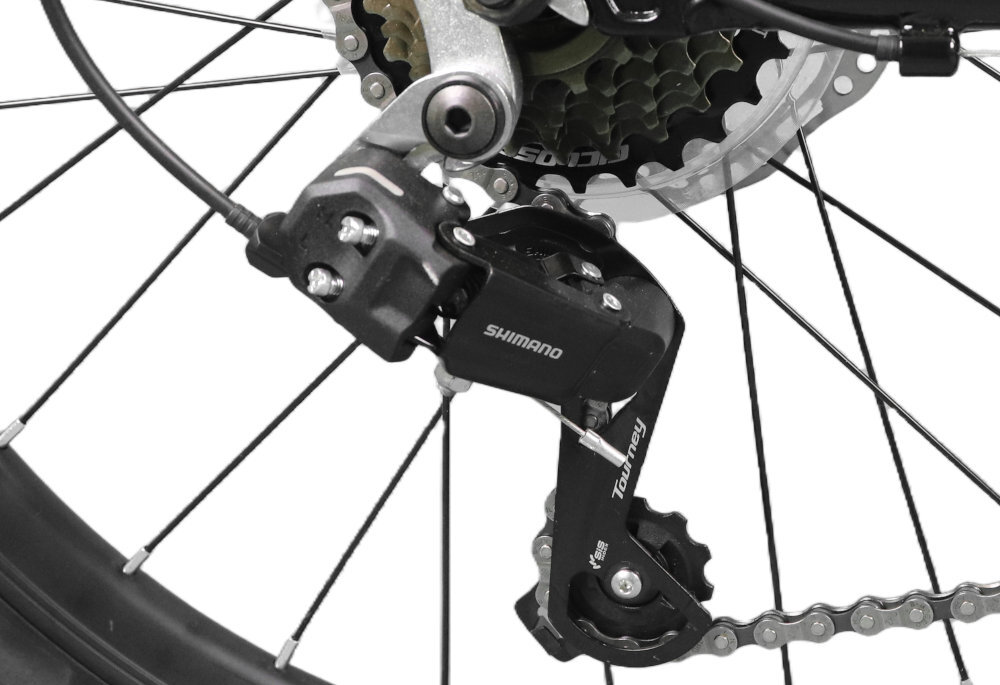 Zdjęcie przedstawia mechanizm przerzutki rowerowej z widocznym napisem \'SHIMANO Tourney\'. Przerzutka jest zamontowana przy kole z zębatkami i łańcuchem.