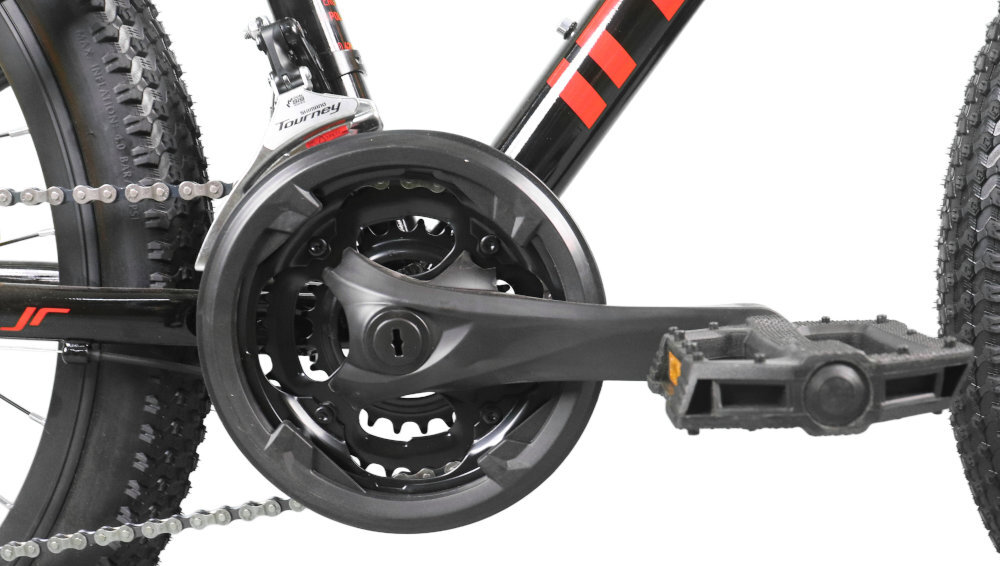 Zbliżenie na mechanizm korbowy roweru z czarno-czerwonymi elementami. Widoczny jest pedał, łańcuch oraz część ramy z napisem \'Tourney\'.