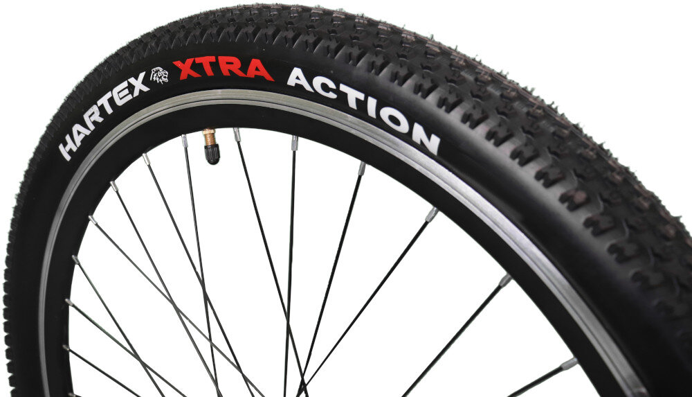 Zbliżenie na oponę rowerową z widocznym napisem \'HARTEX XTRA ACTION\'. Opona ma wyraźny bieżnik i jest zamontowana na metalowej obręczy z szprychami.