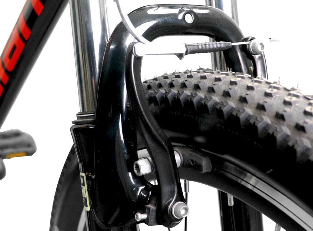 Zbliżenie na przedni hamulec roweru z czarną ramą i grubą oponą z wyraźnym bieżnikiem. Na ramie widoczny jest fragment czerwonego napisu.