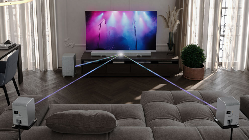 Soundbar SHARP HT-SBW55121 tylne głośniki surround 7.1.4 spójny design, soundbar stojący na komodzie wraz z subwooferem stojącym na podłodze, głosniki rozmieszczone po pokoju skierowane w strone soundbara