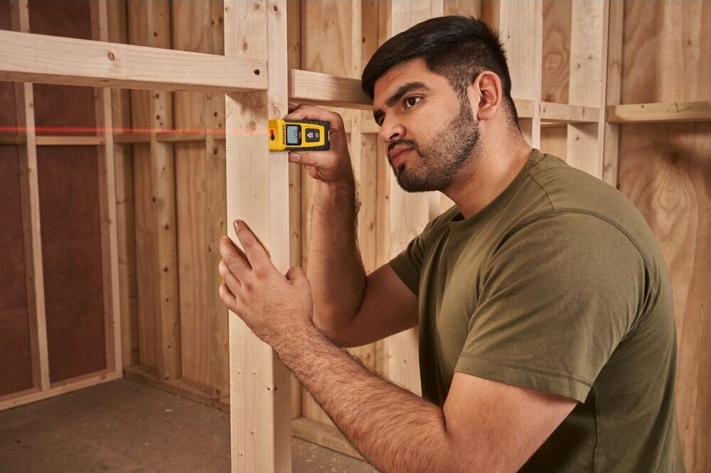 Dalmierz laserowy STANLEY SLM65 STHT77065-0 20m, laser, odległość, precyzja, szybkość, mężczyzna odmierza laserem dystans w pomieszczeniu remontowym