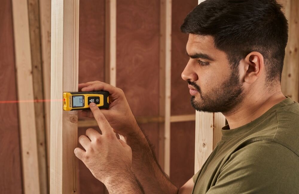 Dalmierz laserowy STANLEY SLM65 STHT77065-0 20m, 2 przyciski, On/Measure, Cog, intuicyjna, mężczyzna wciska przycisk na dlamierzu laserowym