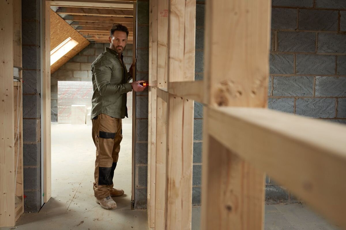 Dalmierz laserowy STANLEY SLM100 STHT77100-0 30m, laser, dwa przyciski, Pitagoras, budowa, mężczyzna odmierza laserem dystans w pomieszczeniu