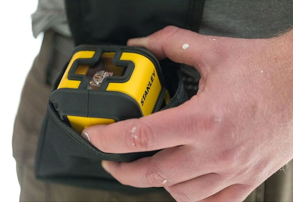 Laser krzyżowy STANLEY STHT77649-1, baterie, ergonomia, mobilność, użytkownicy, Ręka wyjmująca żółtą poziomicę laserową Stanley z czarnego pokrowca przy pasku.