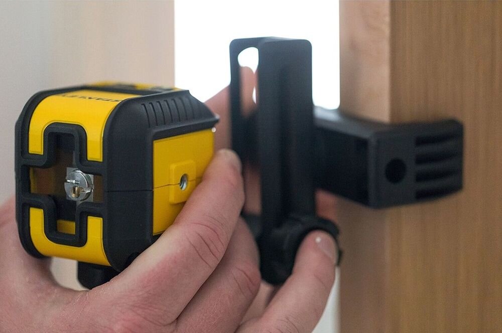 Laser krzyżowy STANLEY STHT77649-1, Quicklink, mocowanie, statyw, stabilność, Montaż poziomicy Stanley na uchwycie przymocowanym do drewnianej ościeżnicy.