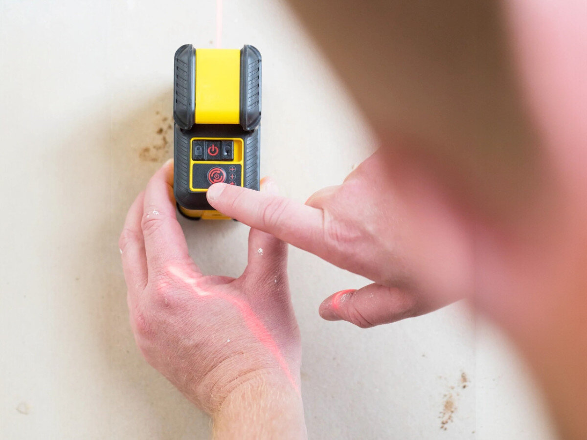 Laser liniowy STANLEY STHT77640-1, linia, pozioma, precyzja, budowa, palec wskazujący przyyciska laser liniowy do ściany