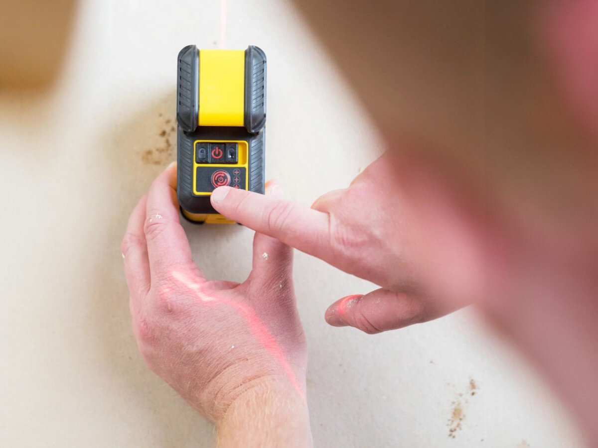 Laser liniowy STANLEY STHT77640-1, linia, pozioma, precyzja, budowa, palec wskazujący przyyciska laser liniowy do ściany