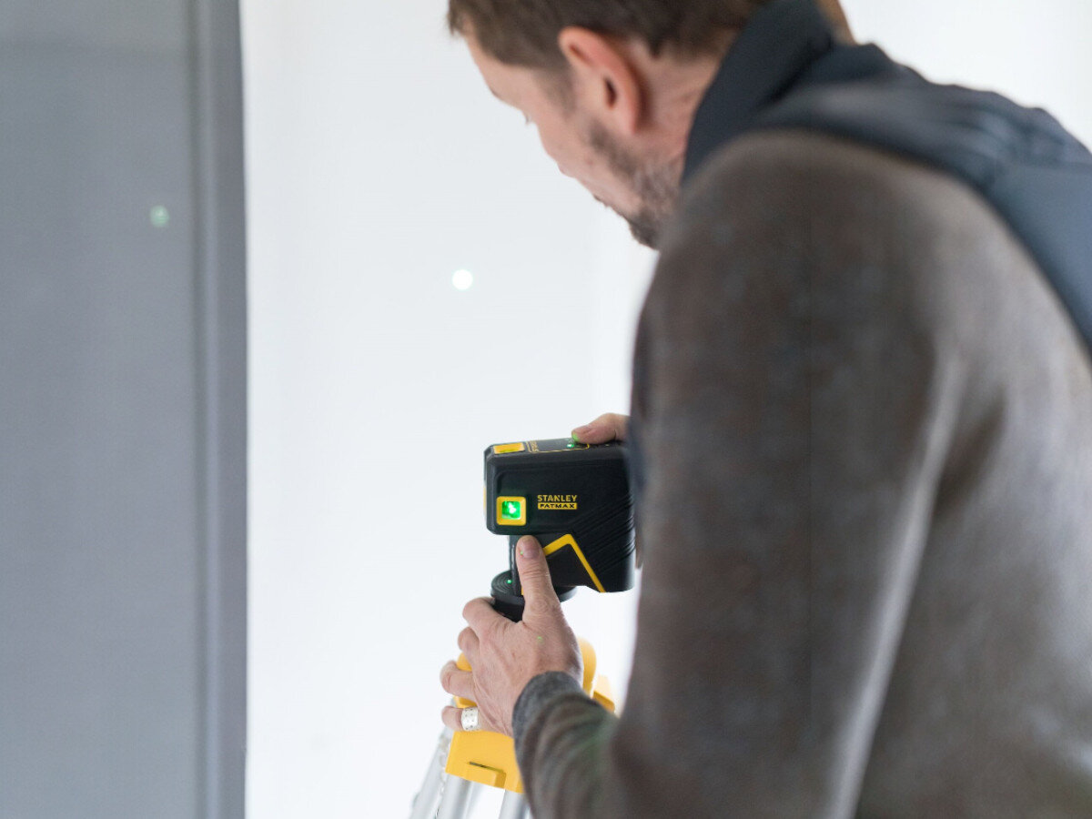 Laser krzyżowy STANLEY Fatmax FMHT77596-1, kąt, pion, budowa, ściana, mężczyzna montuje laser do tripoda